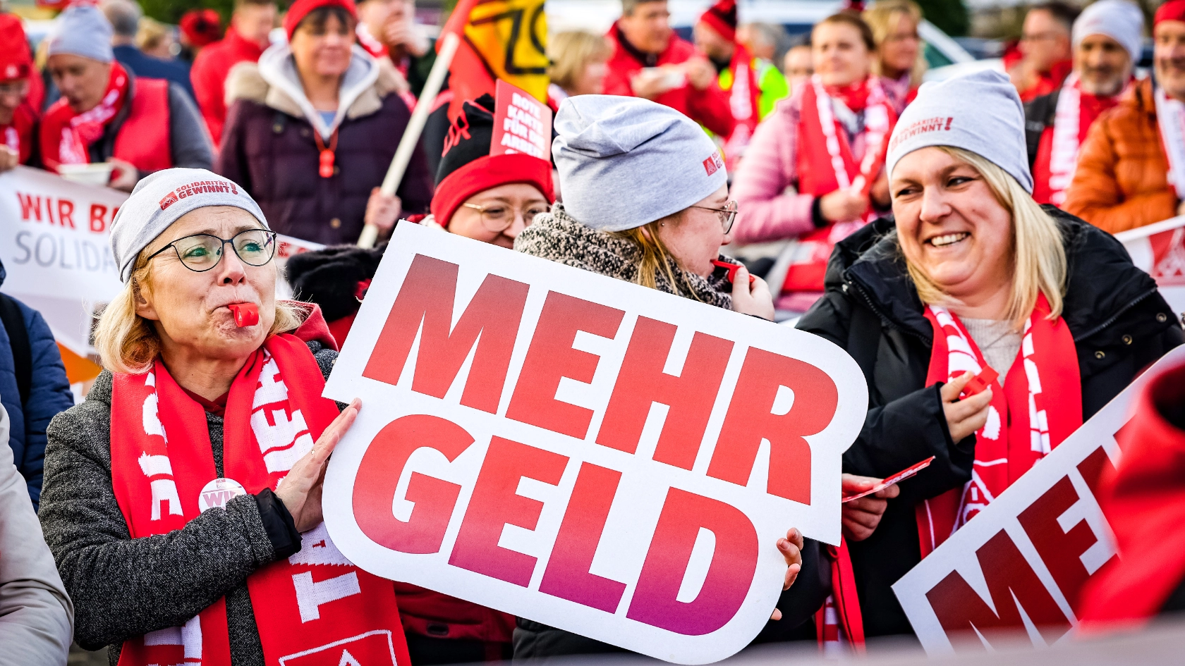 Drei Frauen auf der Demonstration in Kaarst. Eine Frau hält ein Schild „Mehr Geld“ hoch.