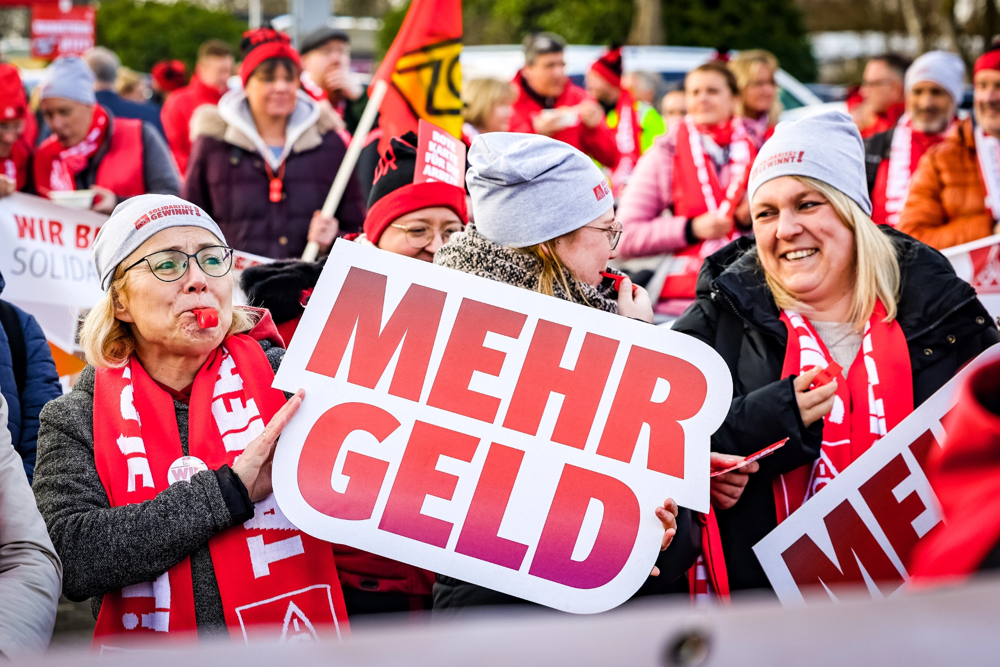 Drei Frauen auf der Demonstration in Kaarst. Eine Frau hält ein Schild „Mehr Geld“ hoch.